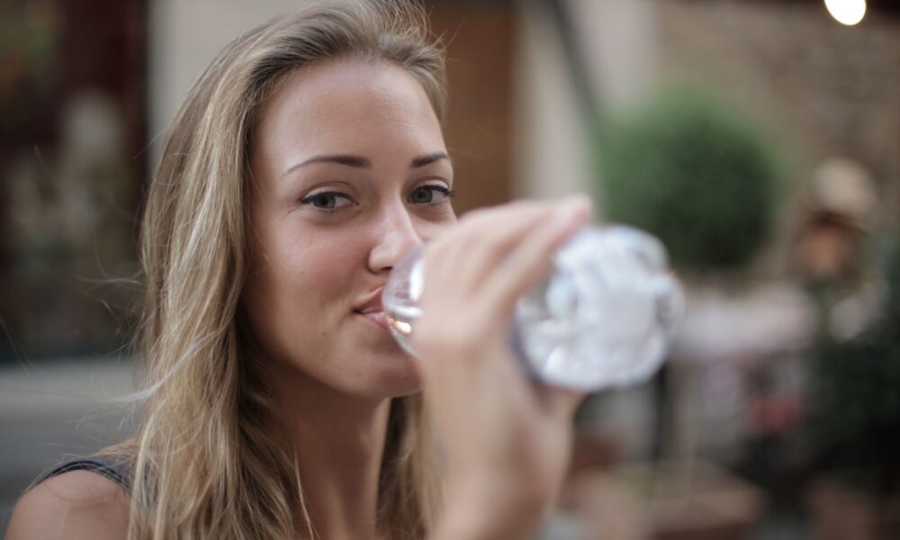 selective focus photo of smiling woman drinking water from a plastic bottle