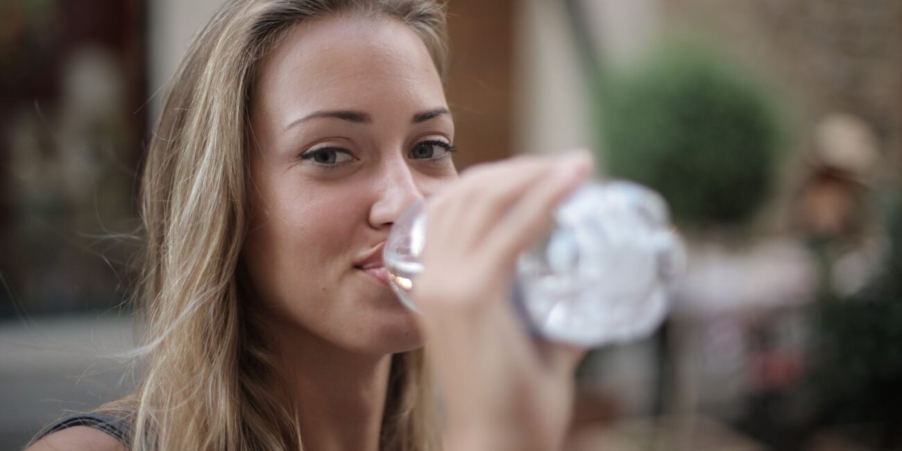 selective focus photo of smiling woman drinking water from a plastic bottle