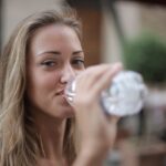 selective focus photo of smiling woman drinking water from a plastic bottle