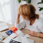 woman sitting next to a laptop with bills and monkey on the table
