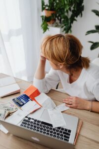 woman sitting next to a laptop with bills and monkey on the table