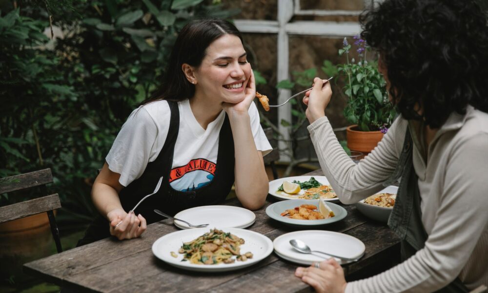 woman feeding girlfriend with fried seafood in garden