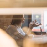 woman in white dress shirt sitting behind a table listening and arguing