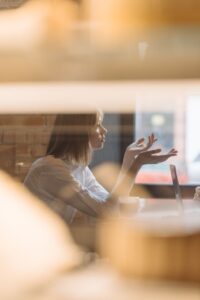 woman in white dress shirt sitting behind a table listening and arguing