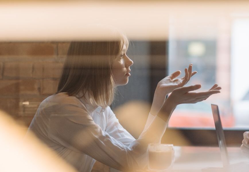 woman in white dress shirt sitting behind a table listening and arguing