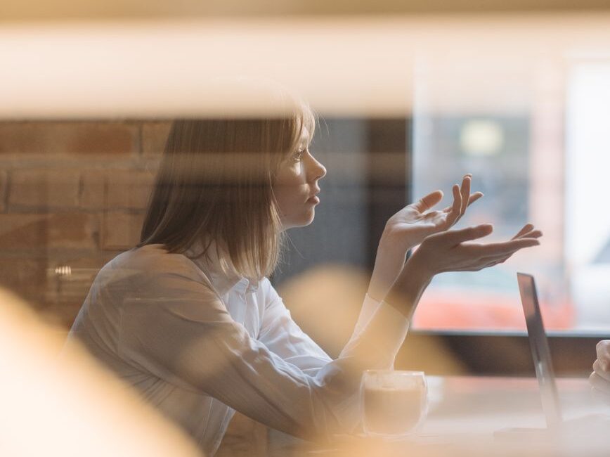 woman in white dress shirt sitting behind a table listening and arguing